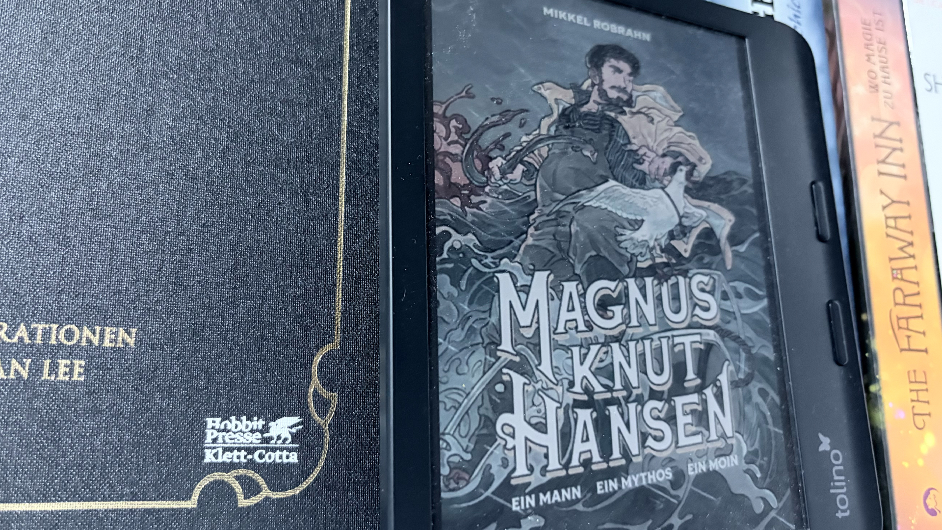 Das Bild zeigt einen Ausschnitt eines Bücherregals in dem ein eReader steht. Auf dem eReader ist das Cover von Magnus Knut Hansen zu sehen.